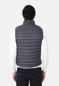Gilet imbottito grigio con trapuntatura orizzontale e colletto alto, indossato su una camicia bianca a maniche lunghe, presenta una vestibilità slim e un design leggero.