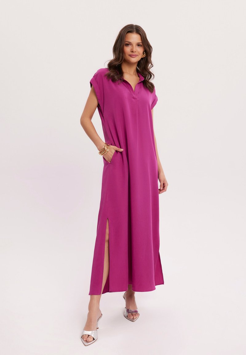 Długa, bezrękawnikowa magentowa sukienka z kołnierzykiem, bocznymi rozcięciami i kieszeniami. Gładka tkanina i luźny krój. Noszona z srebrnymi butami.