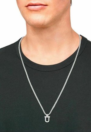 Silberne Kettenhalskette mit einem U-förmigen Anhänger, der eine polierte Oberfläche hat. Die Kette hat ein strukturiertes Gliederdesign und liegt über einem schwarzen Hemd.