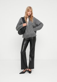Pull en maille gris zippé avec une coupe loose, associé à un pantalon en simili cuir noir à jambes évasées et des escarpins noirs à bout pointu. Simple sac à main noir.
