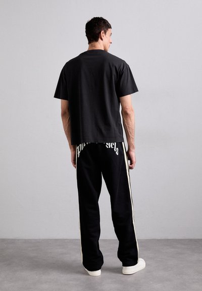 Tricou scurt negru, cu mânecă scurtă și croială lejeră, asociat cu pantaloni de trening negri cu dungi laterale și text grafic pe spate.