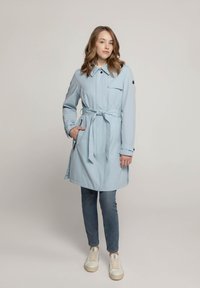 Lichtblauwe, middellange trenchcoat met een ceintuur in de taille, kraag en zijzakken. Gemaakt van zachte stof met knoopaccenten op de mouwen.
