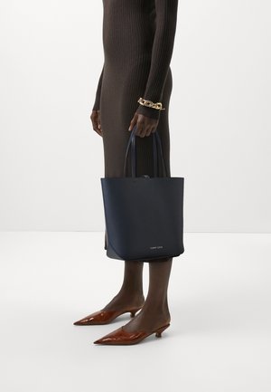 Granatowa skórzana torba tote z dwoma uchwytami o minimalistycznym wzornictwie. Posiada małe logo z przodu, zestawiona z brązowymi szpilkami z wąskim noskiem.