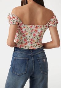 Blommig off-shoulder topp med puffärmar i rosa och vitt, kombinerad med högmidjade blå jeans med en triangel-logopatch på baksidan.