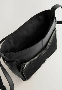 Sac noir composé d'un mélange de cuir lisse et de suède texturé, avec une ouverture zippée et une bandoulière ajustable. L'intérieur est doublé d'un tissu assorti.