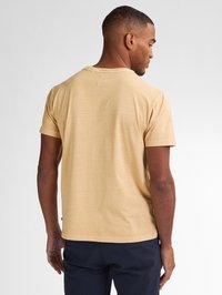 Tricou cu mânecă scurtă, cu decolteu rotund, dintr-un material bej deschis, având o textură ușoară și detalii discrete de cusătură la guler.