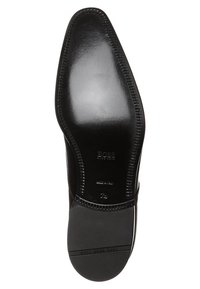 Semelle de chaussure en cuir noir avec une finition lisse, une forme courbée et un bord cousu. Présente des accents en caoutchouc pour une meilleure adhérence. Texte inclus sur la surface.