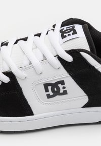 Black and white sneaker featuring a leather and suede upper, white laces, a padded tongue, and a prominent black logo on the side.
