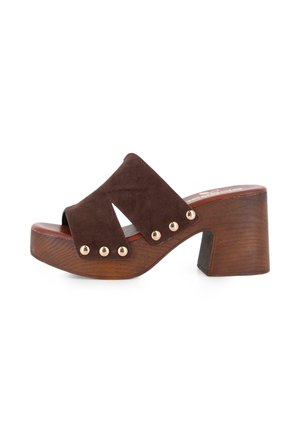 Mule de ante marrón con punta abierta, tacón de bloque de madera y detalles de remaches dorados en las tiras anchas que cubren el pie.