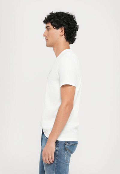 White cotton t-shirt with short sleeves, featuring a crew neckline. Paired with blue denim jeans in a straight cut. Simple design, no patterns.
