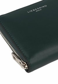 Portefeuille en cuir vert foncé avec une fermeture éclair et des accessoires en argent, logo embossé à l'avant, texture lisse avec des détails de couture précis.