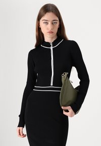 Melna ribota džemperis ar rāvējslēdzēju un baltām akcentējošām svītrām, apvienots ar pieguļošām melnām svārkiem. Modelis tur zaļu somu. Gluda tekstūra, pieguļoša forma.