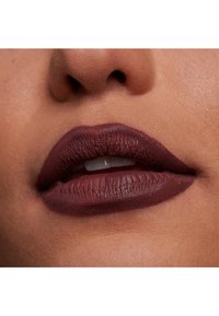 Matte läppstift i en djup burgundnyans, applicerat på fylliga läppar; slät textur med synliga fina linjer och tydliga konturer.