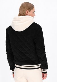 Fekete kordbársony dzseki gyémántmintával, krémszínű plüss kapucnival, bordázott mandzsettával és szegéllyel, fekete-fehér csíkokkal.