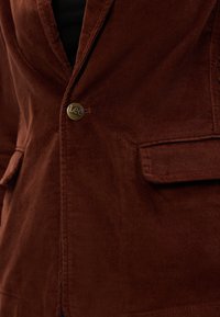 Brun kordfløjl blazer med en enkelt knaplukning med "Lee" indgraveret, to frontlommer og en subtil ribbet tekstur.