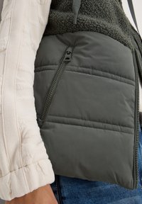 Vadderad väst i mörkgrått tyg med texturerad fleeceöverdel, dragkedjeficka på sidan och kontrasterande ljusfärgad ärmdetalj.