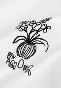 Tela blanca con un jarrón negro bordado con flores. El diseño incluye líneas curvas y texto que dice "ON AMOUR" en estilos variados.