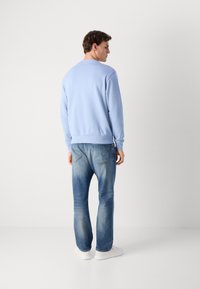 Sudadera azul claro con cuello redondo, puños de canalé, combinada con jeans azul desgastado y zapatillas blancas, vista desde atrás.