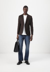 Schwarzer maßgeschneiderter Blazer, weißes T-Shirt, ausgewaschene blaue Jeans, schwarze Lederschuhe und eine schwarze Handtasche. Einfaches, modernes Design. Keine sichtbaren Muster.