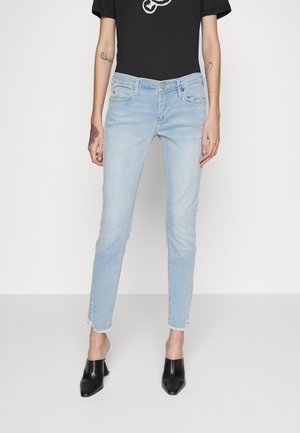 Jean en denim bleu clair avec une coupe ajustée, présentant un ourlet effiloché et un léger décoloration. Associé à un t-shirt graphique noir et des talons noirs.