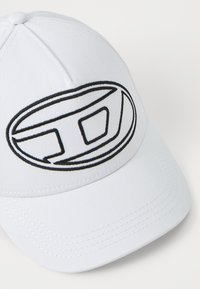 Fehér baseball sapka, kerek, fekete, hímzett logóval. Strukturált fejrésszel és ívelt napernyővel rendelkezik, melyen varrási részletek találhatóak.