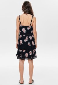 Schwarzes Blumenkleid mit gestuftem Design, verziert mit rosa Rosen, gewellten Trägern und Spitzenverzierungen am Saum. Rückansicht dargestellt.