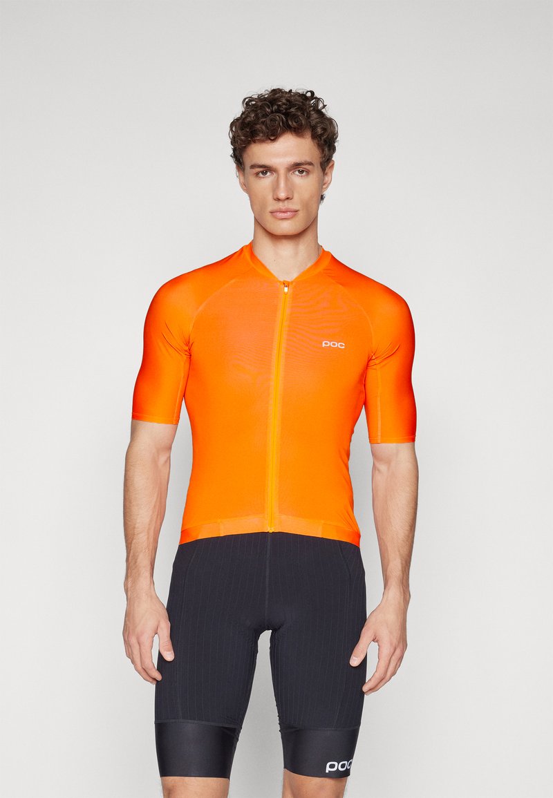 Krátky cyklistický dres z jasne oranžového materiálu, ktorý má predný zips a priliehavý strih. Spárované s čiernymi cyklistickými šortkami so pruhmi.