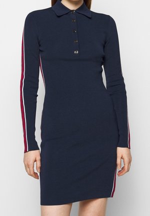 Marineblaues Strickkleid mit langen Ärmeln, Kragen und vier Knöpfen, mit rot-weiß gestreiften Details an Ärmeln und Seiten.