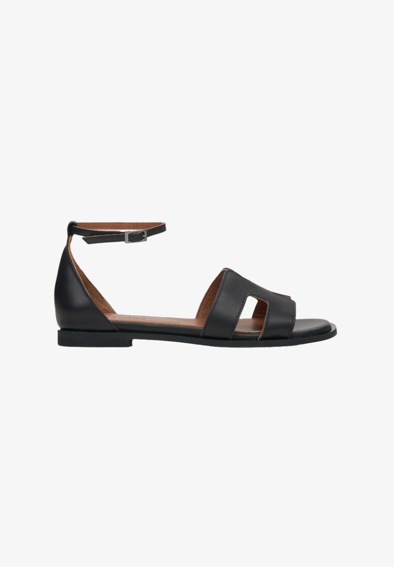 Schwarze Leder-Sandale mit einem Knöchelriemen, offener Spitze und Ausschnittdetails im Oberteil. Flache Sohle mit minimalistischem Design und texture.