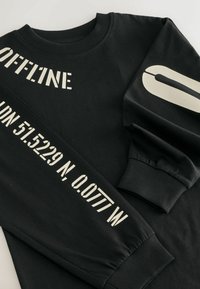 Sort sweatshirt med lange ærmer lavet af bomuld, prydet med hvid tekst "OFFLINE" og geografiske koordinater på ærmerne og fronten.