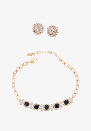 Gouden armband met afwisselend zwarte en heldere edelstenen en gouden oorbellen met een boeket heldere edelstenen in een bloemmotief.
