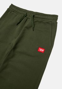 Pantaloni da jogging in cotone verde oliva con vita elastica e cordoncino. Presentano un piccolo patch con logo rosso sul lato sinistro in basso.