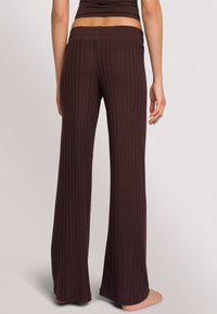 Bruine geribde broek met een brede, elastische tailleband en uitlopende pijpen, met een zachte stofstructuur en verticale patroon.
