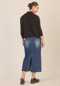 Zwarte gebreide trui met geribde mouwen, gecombineerd met een lange blauwe denim rok met een zijsplits en verspreide versieringen. Dikke zwarte schoenen.