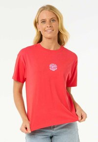 T-shirt en coton rouge à manches courtes, avec un graphisme stylisé blanc sur la poitrine. Coupe décontractée, col rond, texture lisse.