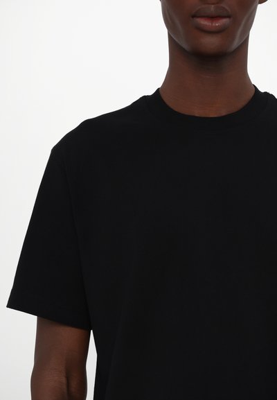Tricou negru cu mânecă scurtă și guler rotund, fabricat dintr-un material de bumbac neted, având cusături curate și o croială relaxată.