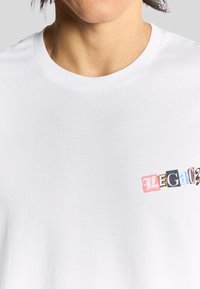 Hvid bomulds t-shirt med et flerfarvet grafisk print med teksten "LEGAL." Rund hals og korte ærmer. Glat tekstur.