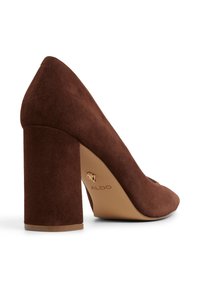 Décolleté in suede marrone con tacco largo, punta affusolata e marchio dorato sulla soletta. Texture liscia e silhouette per un aspetto elegante.