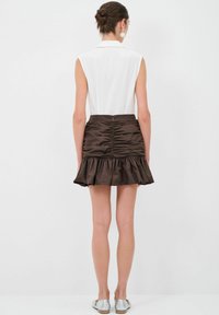 Bílý bezrukávový top, hnědá mini sukně se sklady a volánkovým lemem, hladká textura, zipový uzávěr na zadní straně, modelka má na sobě stříbrné baleríny.