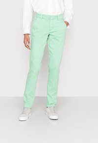 Chinos de algodão verde menta com corte reto, apresentando um cós com passantes para cinto, bolsos laterais e uma textura suave, combinados com ténis brancos.