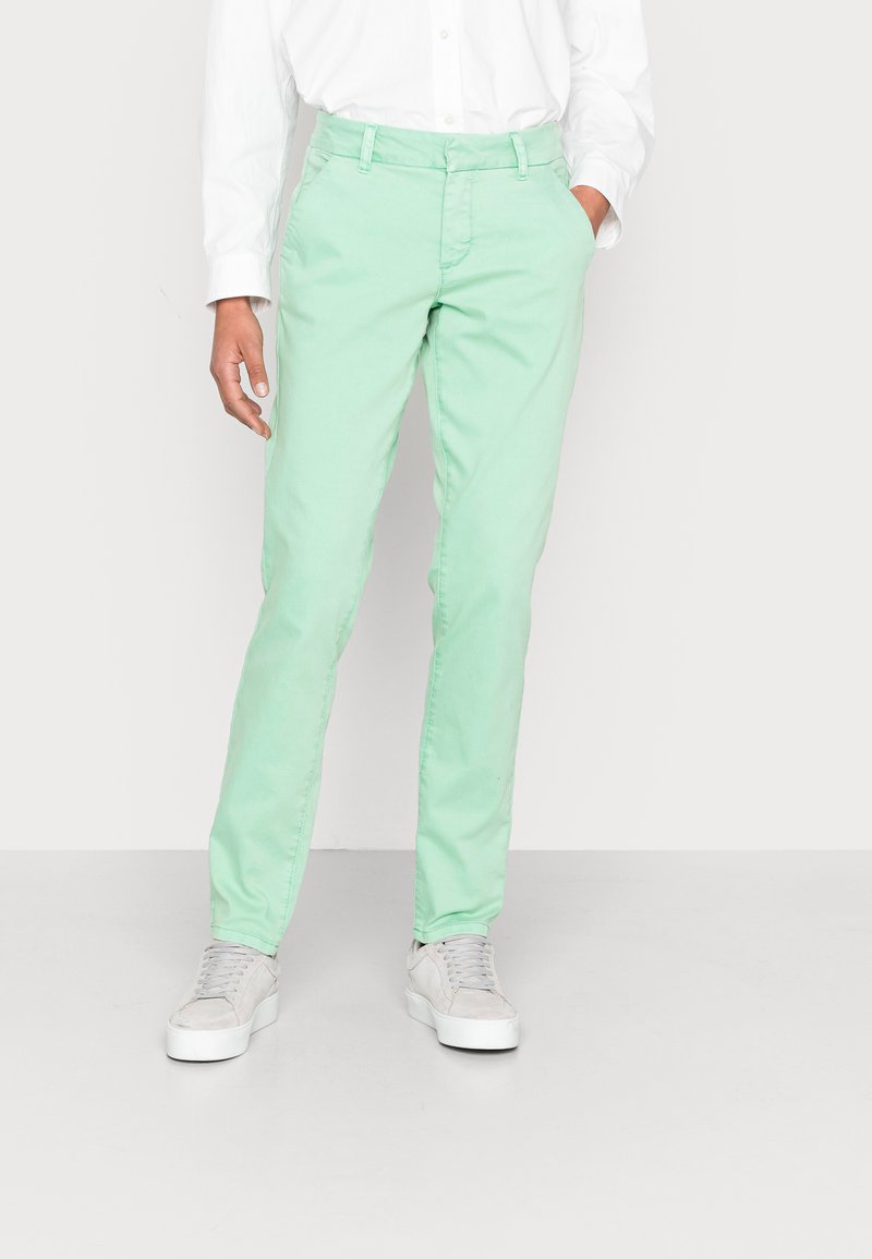 Chinos de algodão verde menta com corte reto, apresentando um cós com passantes para cinto, bolsos laterais e uma textura suave, combinados com ténis brancos.