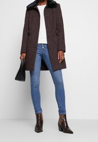 Cappotto in tweed color borgogna scuro con colletto in pelliccia sintetica nera, abbinato a jeans blu e stivali alla caviglia in stampa pitone. Borsa nera.