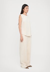 Cream sleeveless top with gathered shoulder detail, paired with wide-leg cream pants and pointed toe shoes featuring a leopard print pattern.