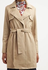 Beige imitationssuede trenchcoat med slagkrage, knytliv och sidofickor. Har en medellång passform och en mjuk textur.