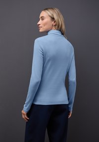 Jasnoniebieski longsleeve z kołnierzem typu turtleneck o dopasowanej sylwetce, faktura prążkowana, prosty dół, w połączeniu z ciemnymi spodniami.