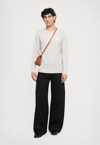 Svetl gray pletený sveter s logom "W", spárovaný s čiernymi širokými cargo nohavicami a malou hnedou crossbody taškou. Jednoduchý dizajn, pohodlný strih.