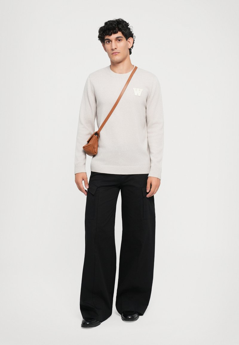 Svetl gray pletený sveter s logom "W", spárovaný s čiernymi širokými cargo nohavicami a malou hnedou crossbody taškou. Jednoduchý dizajn, pohodlný strih.