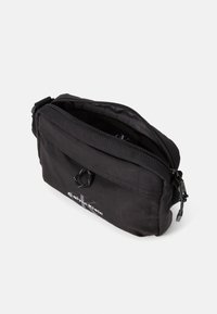 Zwarte stoffen pouch met een bovenrits, voorzien van een voorvak, logo-detail en een ronde trekker. Compact rechthoekig ontwerp.