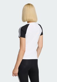 Čiernobiele tričko s krátkym rukávom a raglánovými rukávmi, s čiernymi detailmi na ramenách a tenkými bielymi pruhmi pozdĺž rukávov.