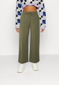 Persoon in olijfgroene wijde broek, witte sneakers en een cropped geblokt sweater in blauw, zwart, lavendel en groen.